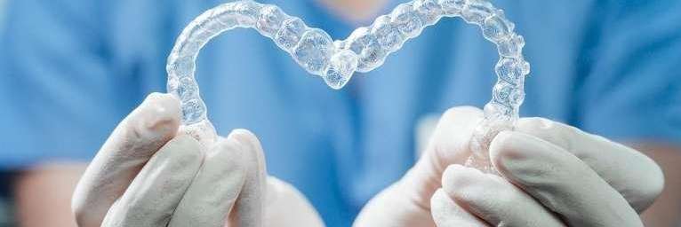 A person holding two Invisalign trays in the shape of a heart