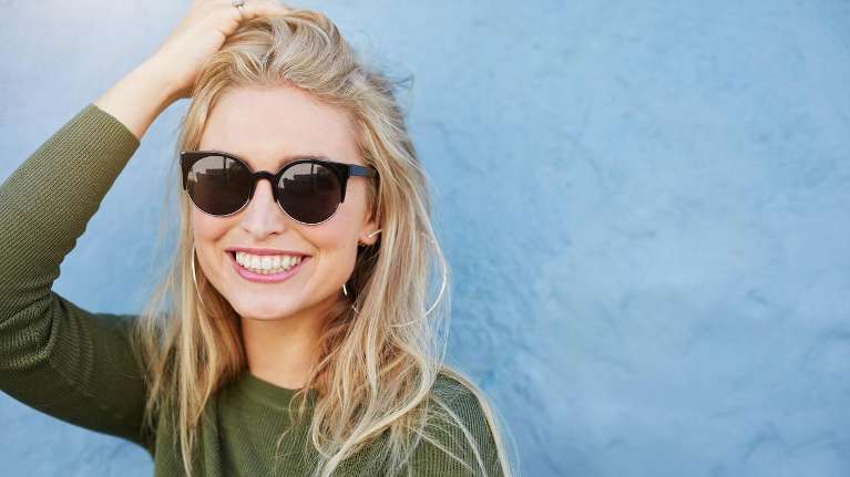 A smiling woman with sunglasses against a blue wall